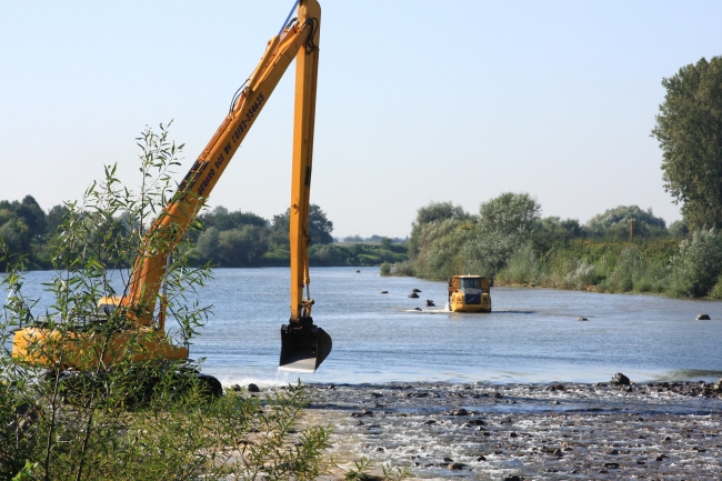 Met dumpers wordt het nodige materiaal voor de aanleg van de drempels naar de plaats van bestemming gereden. In de maas is een soort rijweg uitgezet, gemarkeerd met grote stenen. Met dumpers wordt het nodige materiaal voor de aanleg van de drempels naar de plaats van bestemming gereden. In de maas is een soort rijweg uitgezet, gemarkeerd met grote stenen.
