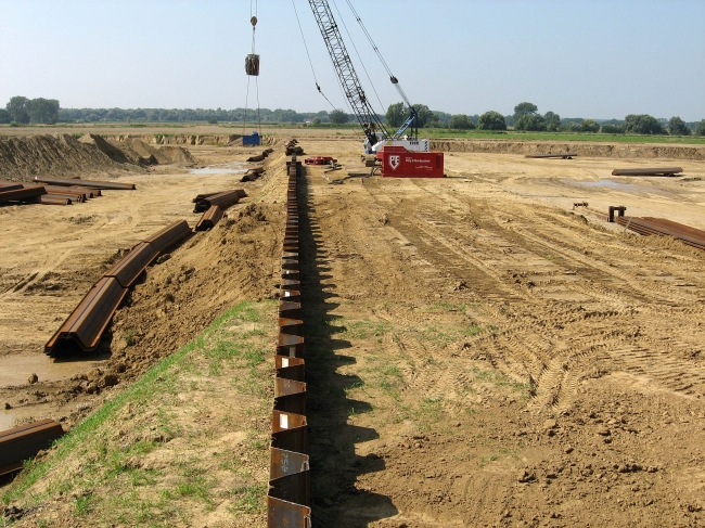 Rechts van de damwanden komt het verwerkingsbekken. Links het zogenaamde voordepot. Hier wordt grind uit de diverse winlocaties gestort waarna het vervolgens vanaf deze plaats via een transportband naar de verwerkingsschepen wordt gebracht om verder verwerkt te worden. Rechts van de damwanden komt het verwerkingsbekken. Links het zogenaamde voordepot. Hier wordt grind uit de diverse winlocaties gestort waarna het vervolgens vanaf deze plaats via een transportband naar de verwerkingsschepen wordt gebracht om verder verwerkt te worden.