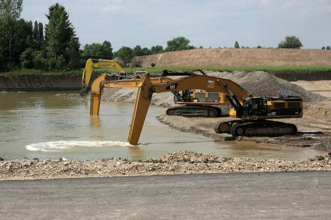 Hier zijn 2 Caterpillar mobiele graafmachines, type 385C en 385C L aan het werk. Dit zjn grote hydraulische graafmachines met een motorvermogen van 530pk. De reikwijdte op maaiveldhoogte bedraagt maar liefst 17,2m en ze kunnen tot op een diepte van maximaal 11.75m het toutvenant naar boven halen. De graafkracht van de bak bedraagt 287kN. Het gewicht van de machine zelf is 88 ton en de bakinhoud kan 3,8m3 bedragen. Het zijn geen snelheidsmonsters, ze halen slechts 4,4 km per uur. Maar hiervoor zijn ze dan ook niet gebouwd. Hier zijn 2 Caterpillar mobiele graafmachines, type 385C en 385C L aan het werk. Dit zjn grote hydraulische graafmachines met een motorvermogen van 530pk. De reikwijdte op maaiveldhoogte bedraagt maar liefst 17,2m en ze kunnen tot op een diepte van maximaal 11.75m het toutvenant naar boven halen. De graafkracht van de bak bedraagt 287kN. Het gewicht van de machine zelf is 88 ton en de bakinhoud kan 3,8m3 bedragen. Het zijn geen snelheidsmonsters, ze halen slechts 4,4 km per uur. Maar hiervoor zijn ze dan ook niet gebouwd.