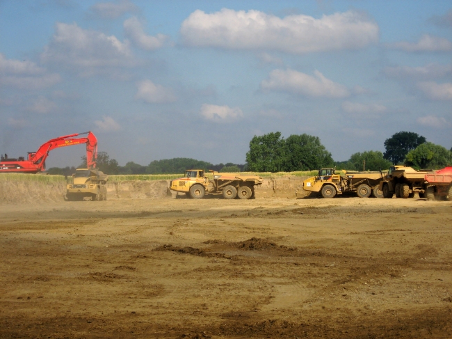 Dumpers staan in de rij om grond te laden. De grond wordt opgeslagen in het gronddepot ten noorden van Itteren. Iedere twee minuten wordt er ca 35 ton grond weggebracht.
