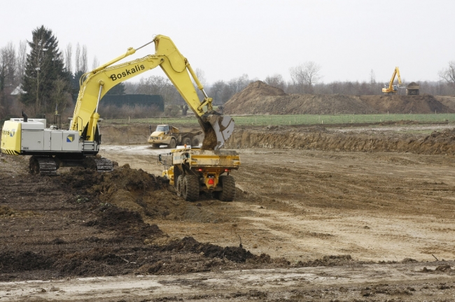 De kiezel zit hier minder diep zodat er minder hoeft te worden afgegraven. Per dag wordt zo'n 2500 tot 3000 m3 grond verzet. Aan de rechterkant ziet u het gronddepot waar de afgegraven grond wordt opgeslagen. Het gronddepot doet tevens dienst als geluidswal.