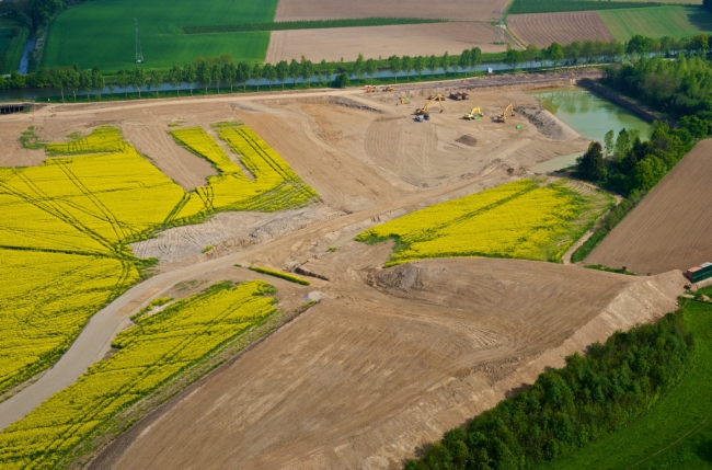 Op de voorgrond het gronddepot dat tevens dienst doet als geluidsscherm. Bovenaan rechts is men al begonnen met dieper te graven om grind te winnen voor de aanleg van de werkwegen en het op hoogte brengen van het grintdepot voor de opbouw van de technische installaties.