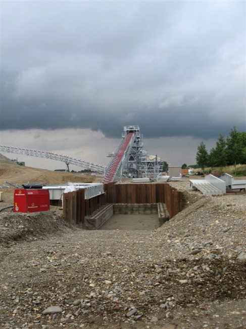 Het aangevoerde grind wordt links in de witte bak gestort. Te grote stukken worden verwijderd (> 30 cm) en rechts in de Het aangevoerde grind wordt links in de witte bak gestort. Te grote stukken worden verwijderd (> 30 cm) en rechts in de