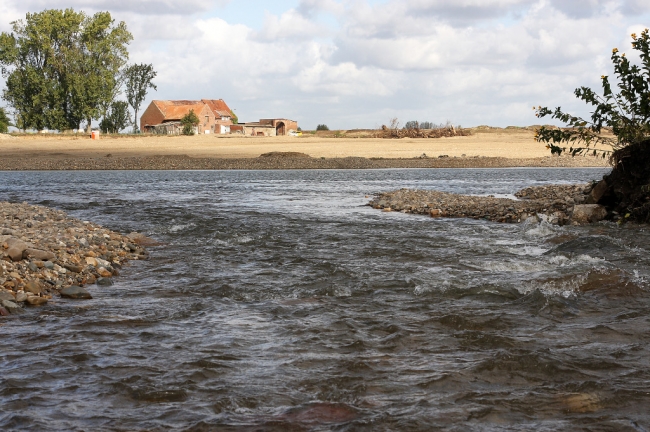 Foto van de oeververlaging in Herbricht, genomen vanuit de monding van de Geul in de Maas. Op de achtergrond de boerderij van de familie Eurlings.