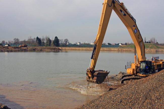 Rechts wordt de toutvenant uit de diepte opgehaald en links wordt de dekgrond alweer gestort waar de kiezel uit de ondergrond al is gewonnen. Achterdoor de woningen van Op de Hoogmaas. Rechts wordt de toutvenant uit de diepte opgehaald en links wordt de dekgrond alweer gestort waar de kiezel uit de ondergrond al is gewonnen. Achterdoor de woningen van Op de Hoogmaas.