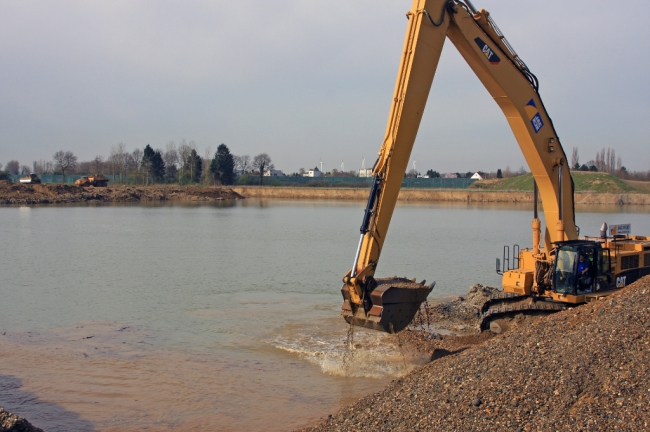 Rechts wordt de toutvenant uit de diepte opgehaald en links wordt de dekgrond alweer gestort waar de kiezel uit de ondergrond al is gewonnen. Achterdoor de woningen van Op de Hoogmaas. 