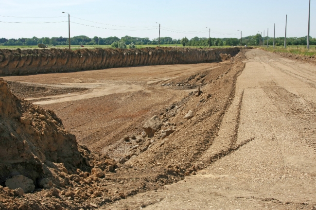 Links bij de lantaarnpalen loopt nog de oude weg naar Herbricht. Inmiddels is men al vergevorderd met de aanleg van de nieuwe weg meer landinwaarts, rechts op de foto. Het gedeelte links van de nieuwe weg zal ook worden afgegraven in het kader van de oeververbreding van de Maas. 