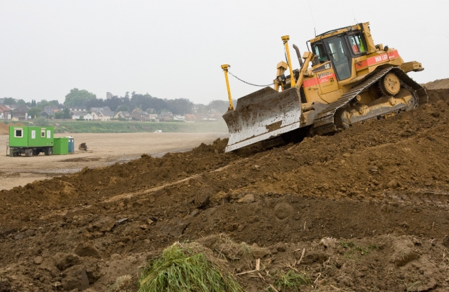 Bulldozer bezig met het afgraven van de recent aangelegde geluidswal langs de Maas in Borgharen. De grond wordt gebruikt om de oever schuin af te werken. Als deze losse grond niet voor de winter stevig begroeid is weet de Maas er wel raad mee. 