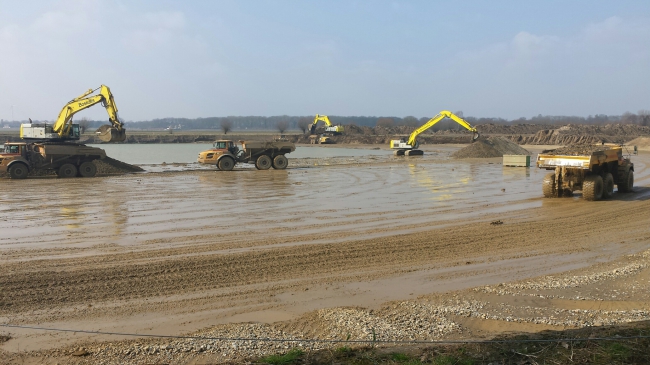Er wordt met man en macht gewerkt. Er is sprake van zowel het verwijderen van de dekgrond (op de achtergrond) als grindwinning. Na de zomer moet het werk zijn afgerond en kan begonnen worden met de afbouw (verwijderen werkweg en werkbrug). Er wordt met man en macht gewerkt. Er is sprake van zowel het verwijderen van de dekgrond (op de achtergrond) als grindwinning. Na de zomer moet het werk zijn afgerond en kan begonnen worden met de afbouw (verwijderen werkweg en werkbrug).