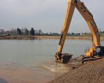 Rechts wordt de toutvenant uit de diepte opgehaald en links wordt de dekgrond alweer gestort waar de kiezel uit de ondergrond al is gewonnen. Achterdoor de woningen van Op de Hoogmaas.  (7-4-2010 - Jan Dolmans)