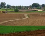 Op de voorgrond is de dekgrond al verwijderd. De akkers links van de afrastering behoren tot de onvergraven natuur. In de verte wordt gewerkt aan de stroomgeulverbreding. Op de achtergrond het gehucht Herbricht.  (4-5-2010 - Jan Dolmans)