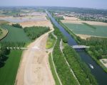 Luchtfoto van de werkweg bij Op de Bos te Itteren met rechts het Julianakanaal en aan de bovenzijde het reeds gedeeltelijk ontgrinde Hartelsteinerveld. Op deze luchtfoto ziet u duidelijk dat achter de bomenrij in het midden van de foto de dekgrondberging al weer gedeeltelijk is opgevuld. Ter hoogte van de brug over het Julianakanaal, midden op de foto, is een ongelijkvloerse kruising gemaakt waarbij het werkverkeer over de bestaande weg heen gaat.  (5-6-2010 - Ralph Faun )