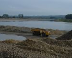 Dumpers vervoeren de afgegraven dekgrond naar de dekgrondberging. De waterplas op de achtergrond geeft het beeld weer dat ons waarschijnlijk te wachten staat. De graafmachines hebben hier al tot op een diepte van 36m boven NAP de kiezel weggegraven.  (27-9-2010 - Reen van Beek)