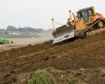 Bulldozer bezig met het afgraven van de recent aangelegde geluidswal langs de Maas in Borgharen. De grond wordt gebruikt om de oever schuin af te werken. Als deze losse grond niet voor de winter stevig begroeid is weet de Maas er wel raad mee.  (20-5-2011 - Jan Dolmans)